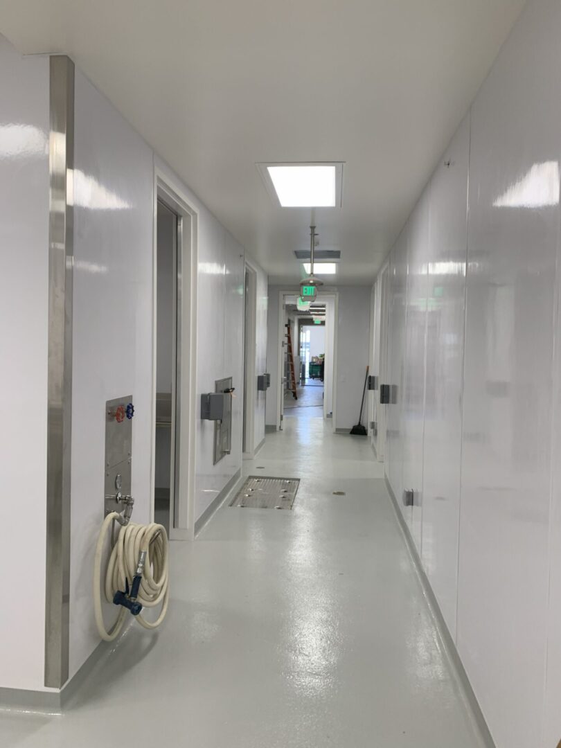 A clean, white corridor with doors and utility equipment along the walls.