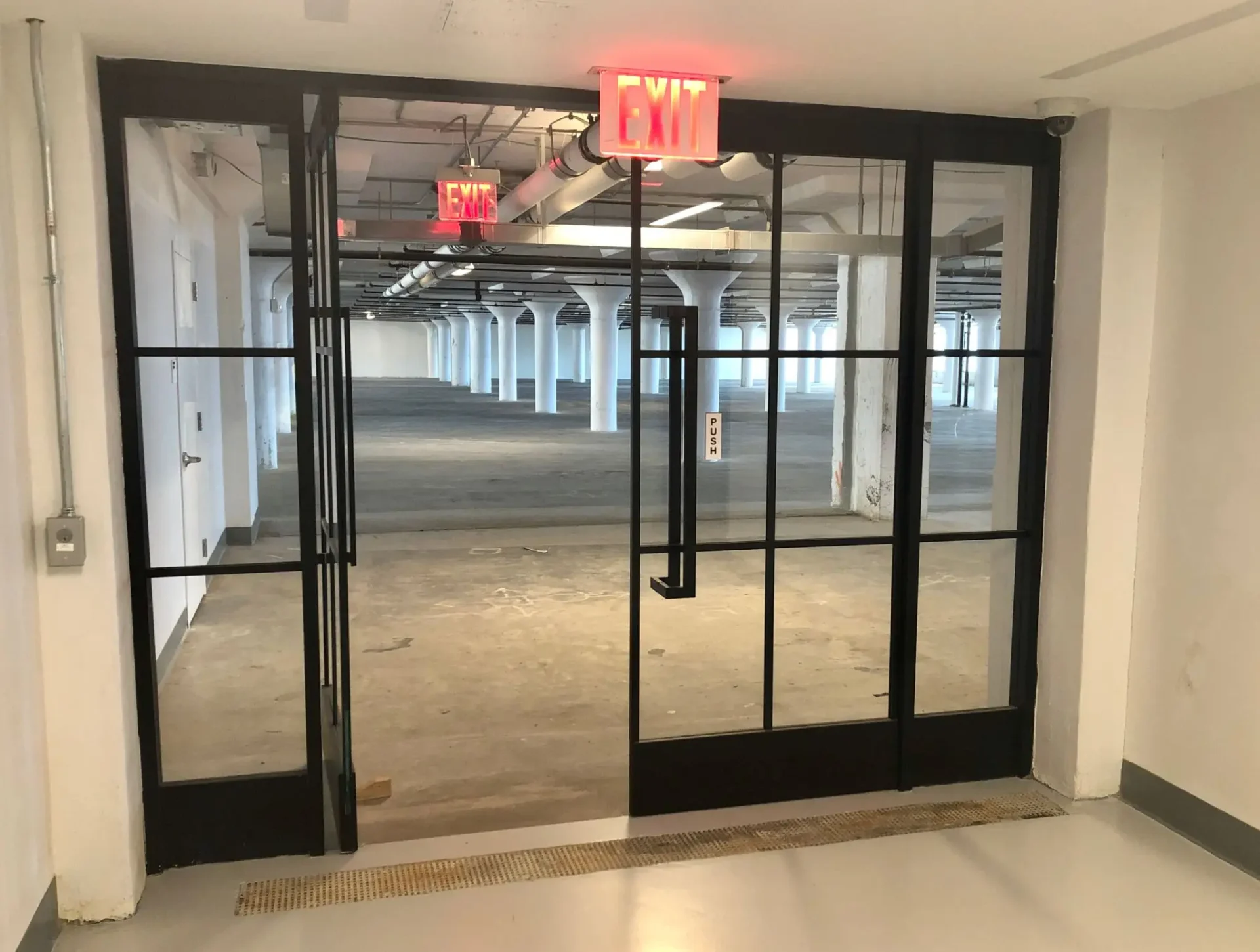 Modern glass doors leading to a spacious, empty office corridor.